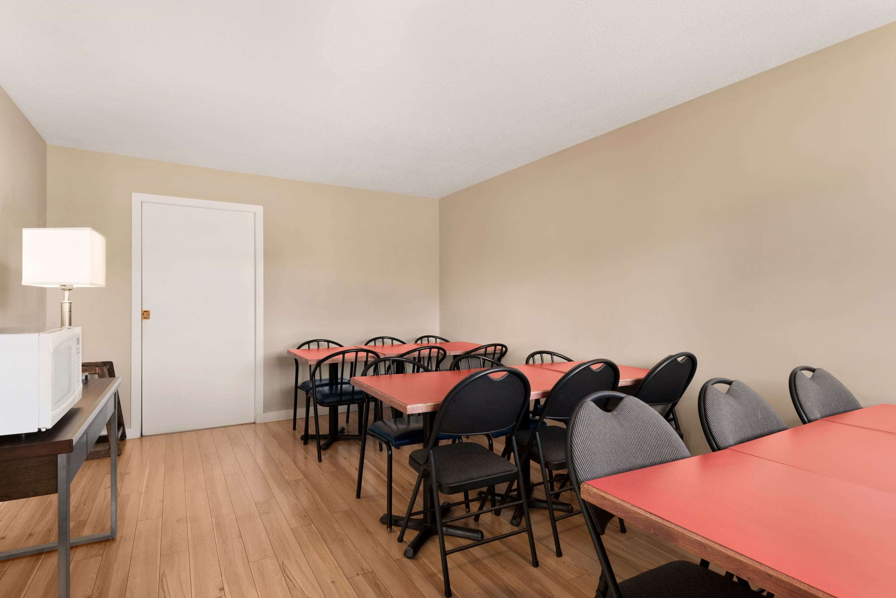 A conference room with wooden floors, beige walls, and red tables with black chairs.