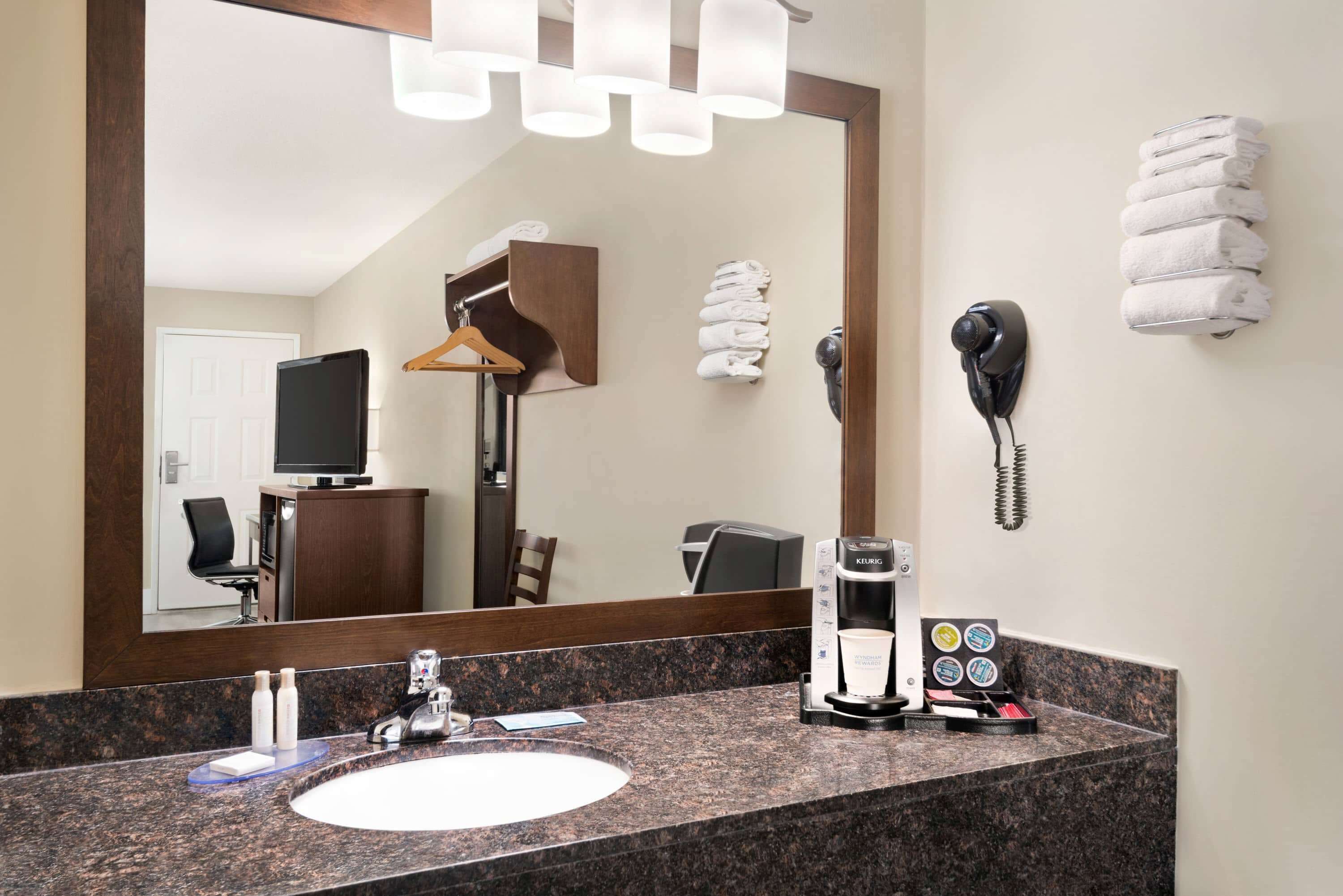 A hotel bathroom with a granite countertop, a sink, a mirror, a towel rack, a telephone, and a coffee maker.