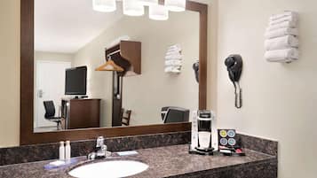 A hotel bathroom with a granite countertop, a sink, a mirror, a towel rack, a telephone, and a coffee maker.
