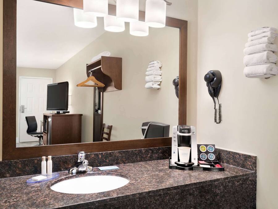 A hotel bathroom with a granite countertop, a sink, a mirror, a towel rack, a telephone, and a coffee maker.