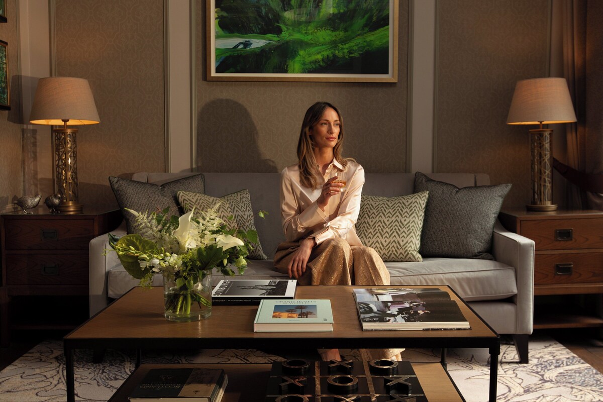 A woman sitting on a sofa in a well-lit room with a coffee table, books, and decorative items.