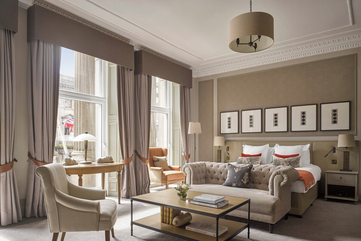 A spacious living room with a large window, a sofa, a coffee table, and a chandelier.