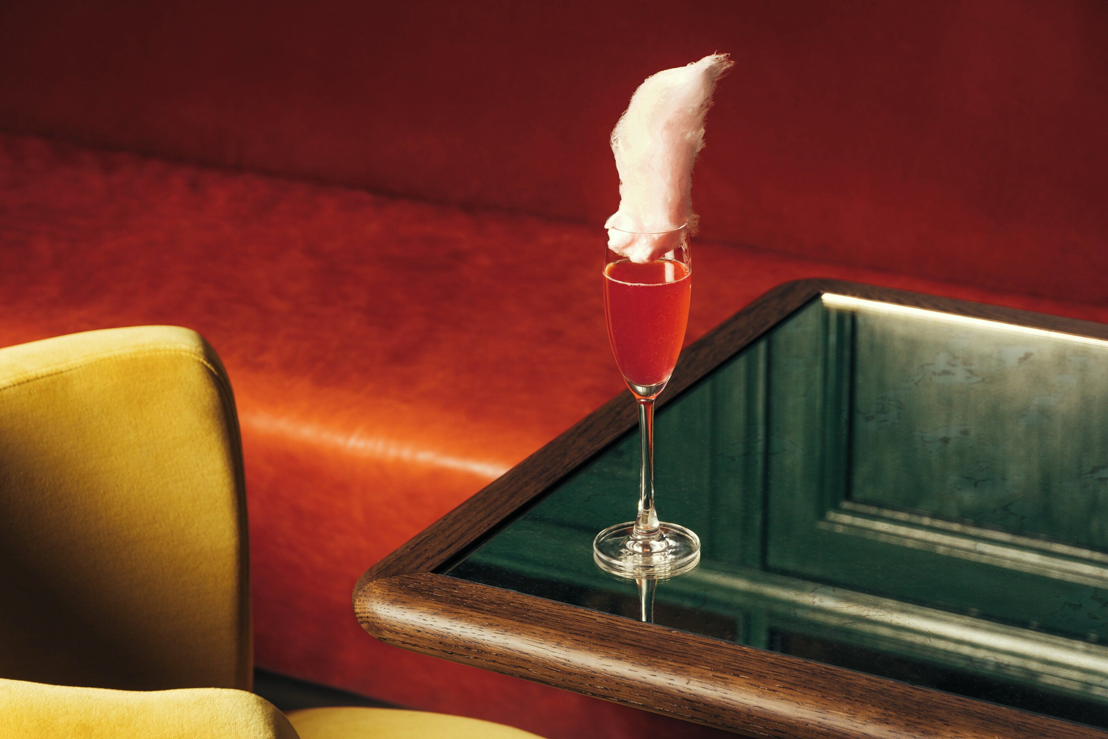 A cocktail glass with a white napkin on a wooden table against a red wall.