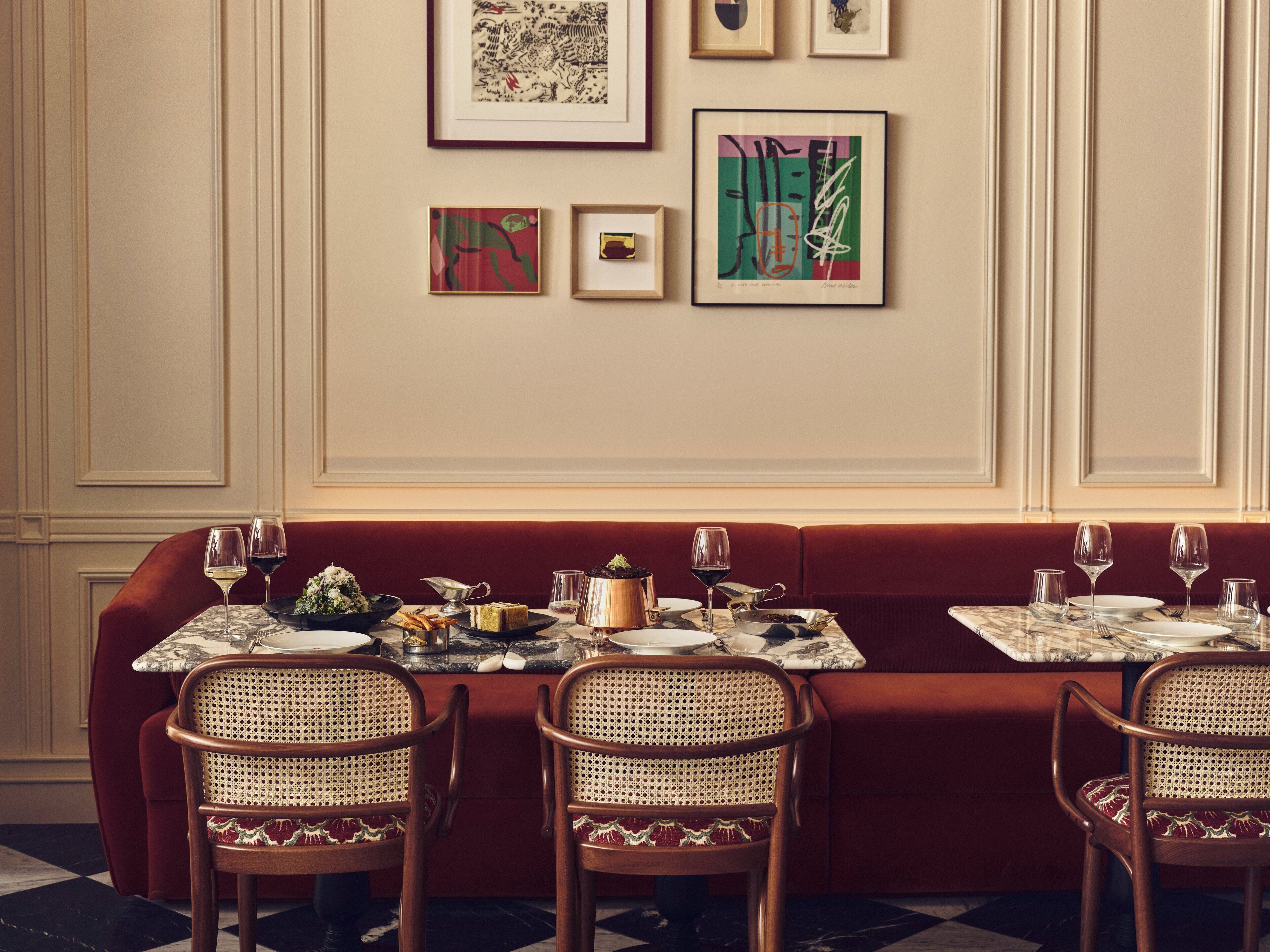 A dining area with a red upholstered booth, a marble table, and wicker chairs.