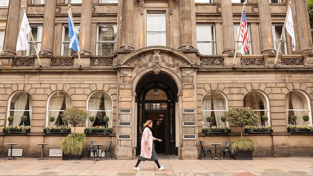 A historic building with a grand entrance, multiple flags, and outdoor seating.