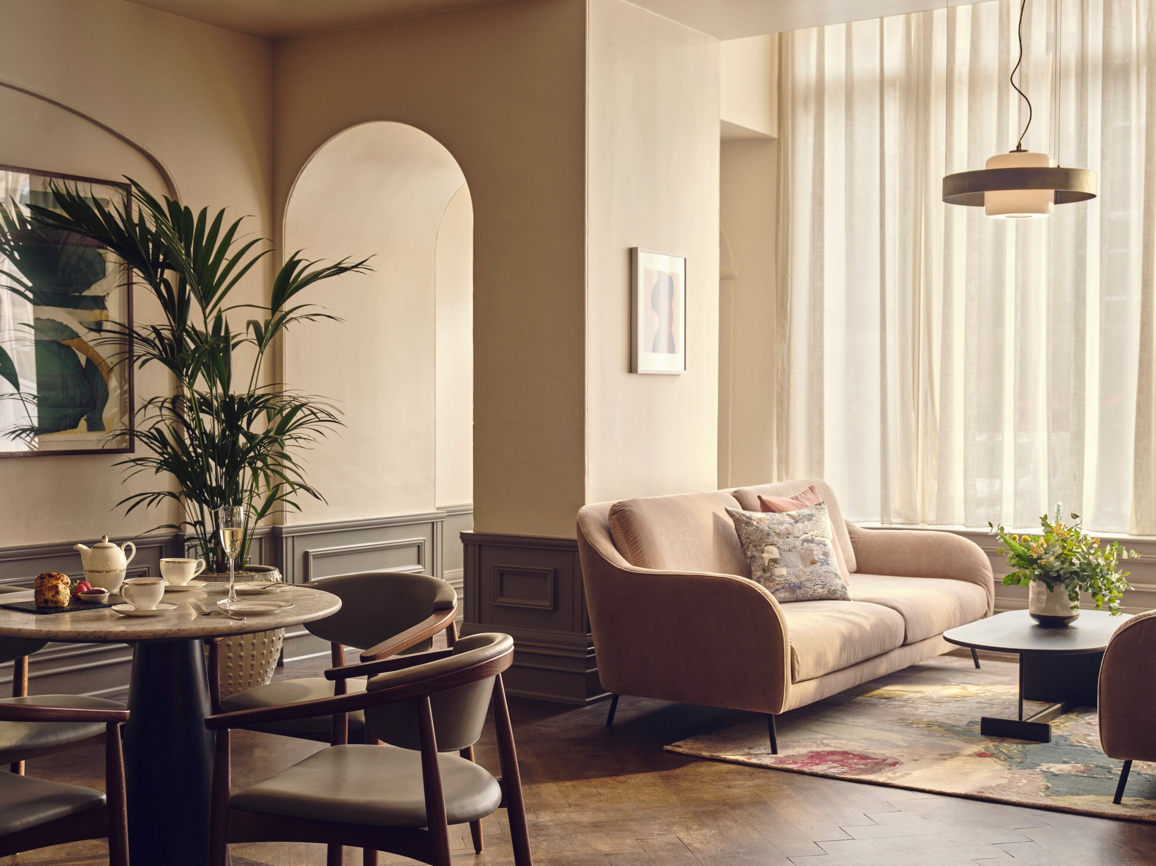 Una sala de estar con un sofá color beige, una mesa de centro redonda y un comedor con sillas y una mesa dispuesta para una comida.