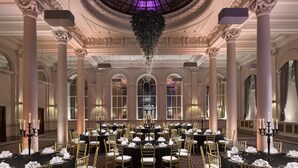 A grand banquet hall with ornate columns, a high ceiling with a glass dome, and tables set for a formal event.