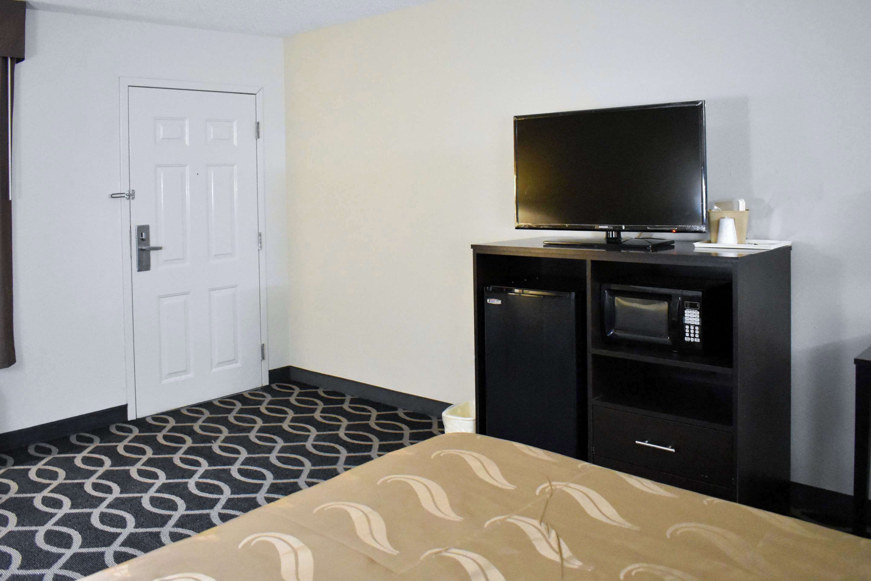 Een hotelkamer met een bed, een televisie, een magnetron en een klein kastje.