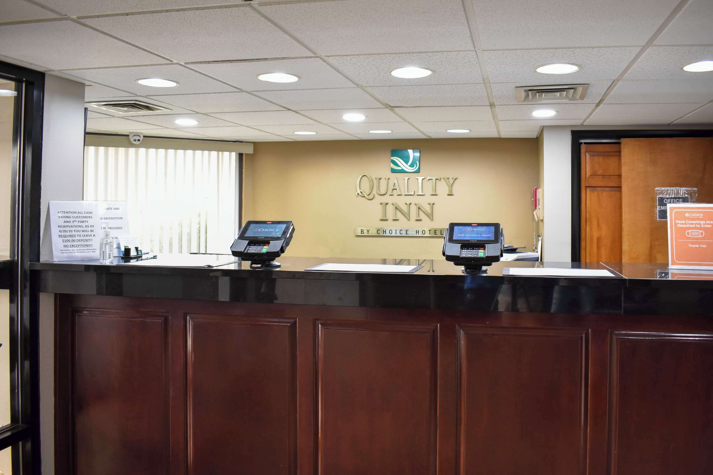 En receptionsdisk på Quality Inn med en logotyp, två datorstationer och en skylt som visar var kontorsområdet ligger.