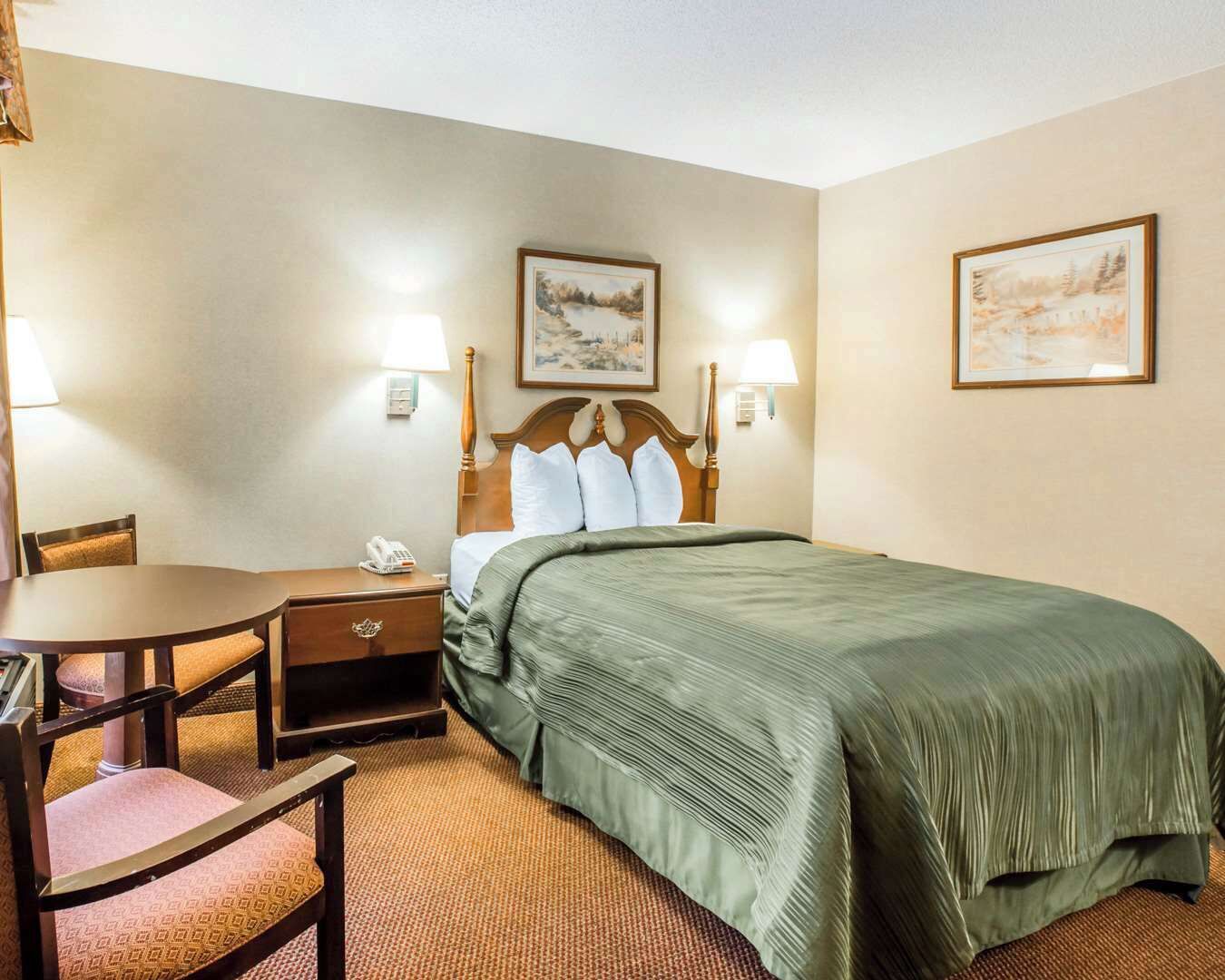 A hotel room with a bed, a desk, a chair, and two wall-mounted lamps.