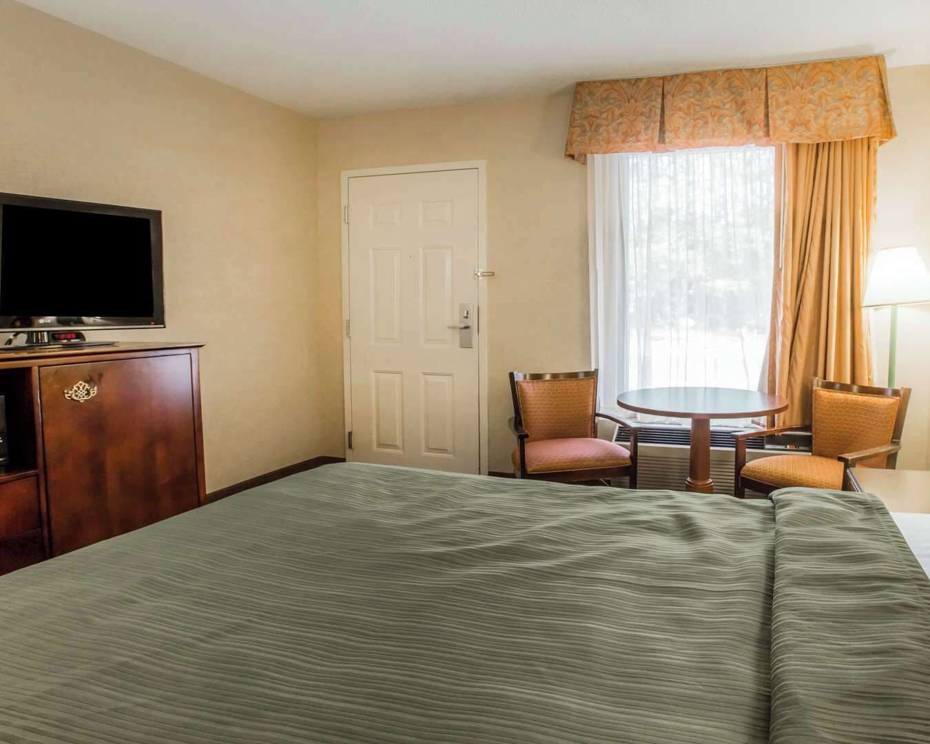 Habitación de hotel con cama, televisión sobre un mueble, escritorio con silla y ventana con cortinas.