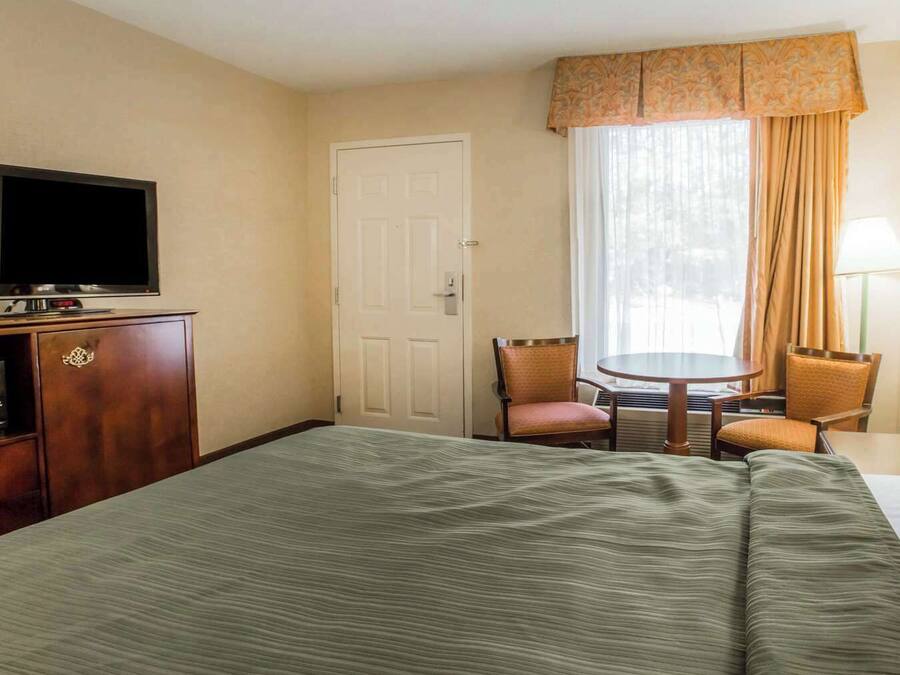 Habitación de hotel con cama, televisión sobre un mueble, escritorio con silla y ventana con cortinas.