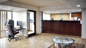 A hotel reception area with a wooden reception desk, a computer, and a glass-top table. - Quality Inn Reidsville Hwy 29 (Reidsville)