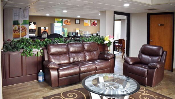 A lobby with a brown leather sofa, a glass coffee table, and a brown leather armchair. There is a reception desk with a plant barrier in the background. - Quality Inn Reidsville Hwy 29 (Reidsville)
