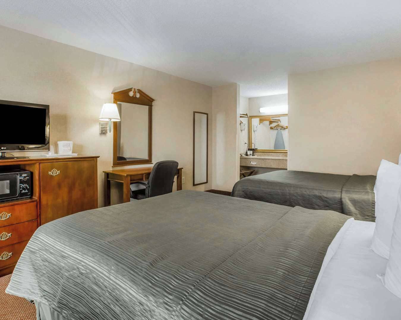 A hotel room with two beds, a desk with a chair, a television, and a mirror.