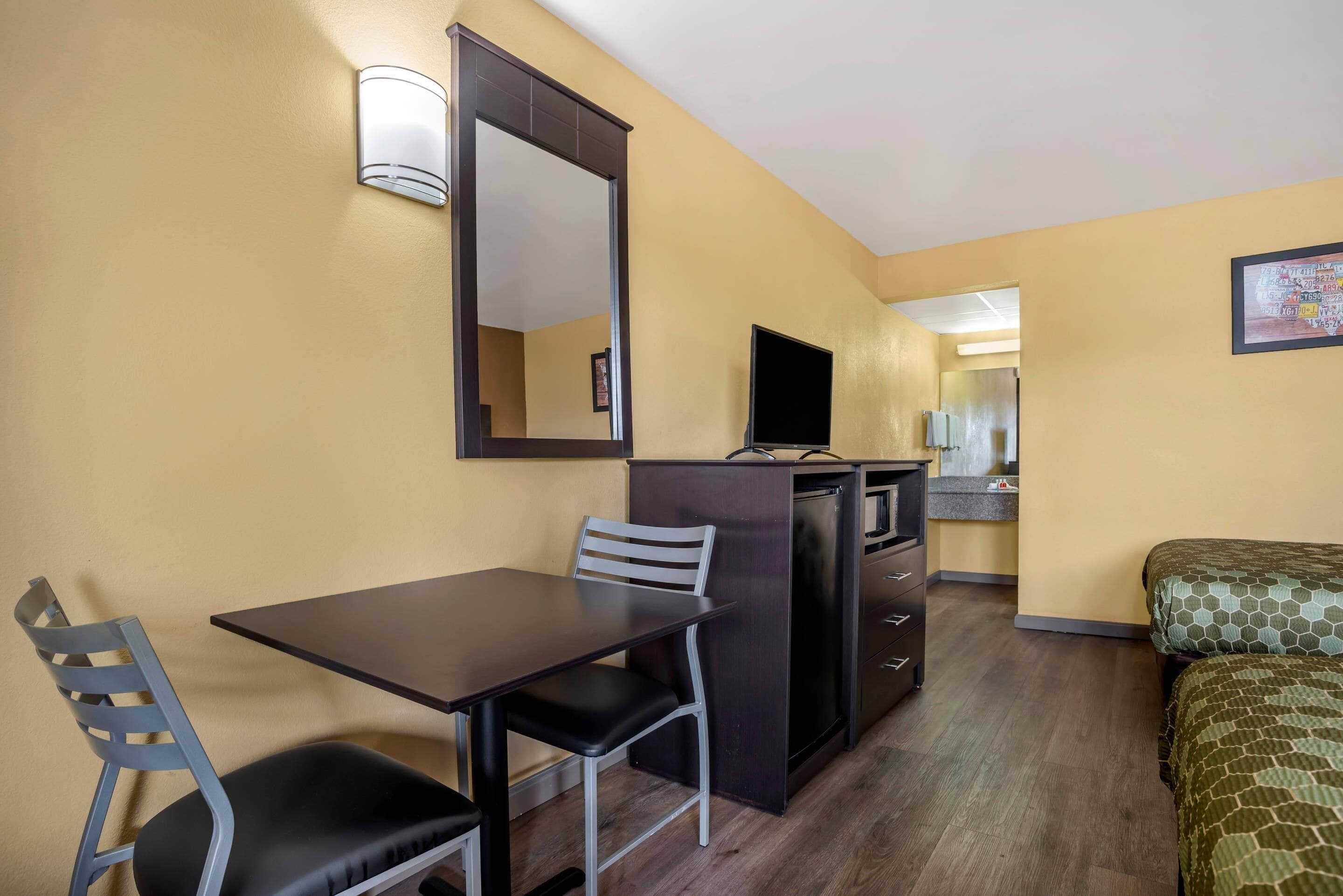A compact hotel room with a single bed, a small desk with a chair, a TV, and a kitchenette.