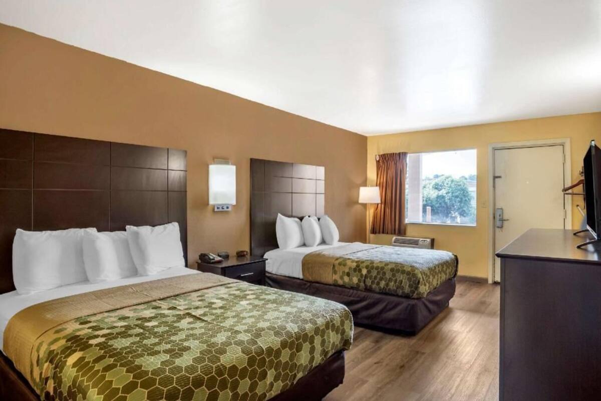 Ein Hotelzimmer mit zwei Betten, einem Schreibtisch, einem Fernseher und einem Fenster.