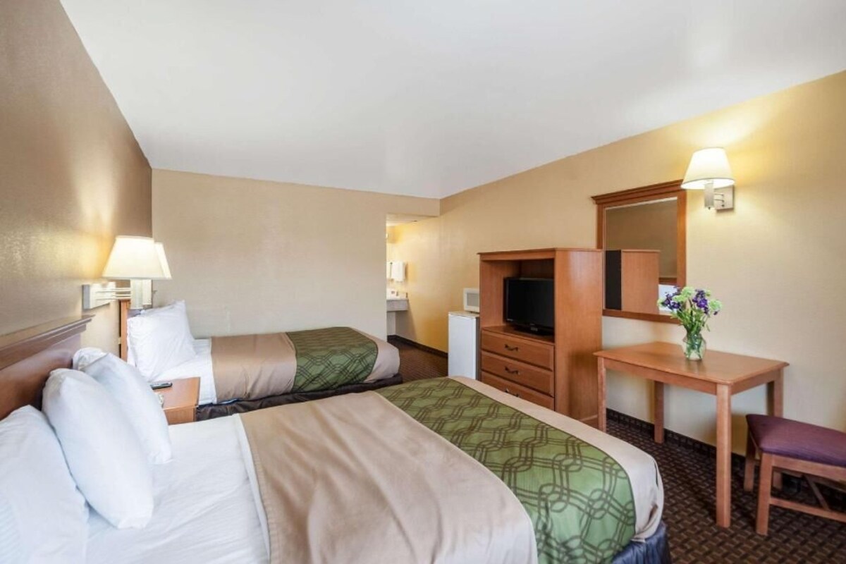 A hotel room with two beds, a desk, a TV, and a mirror.