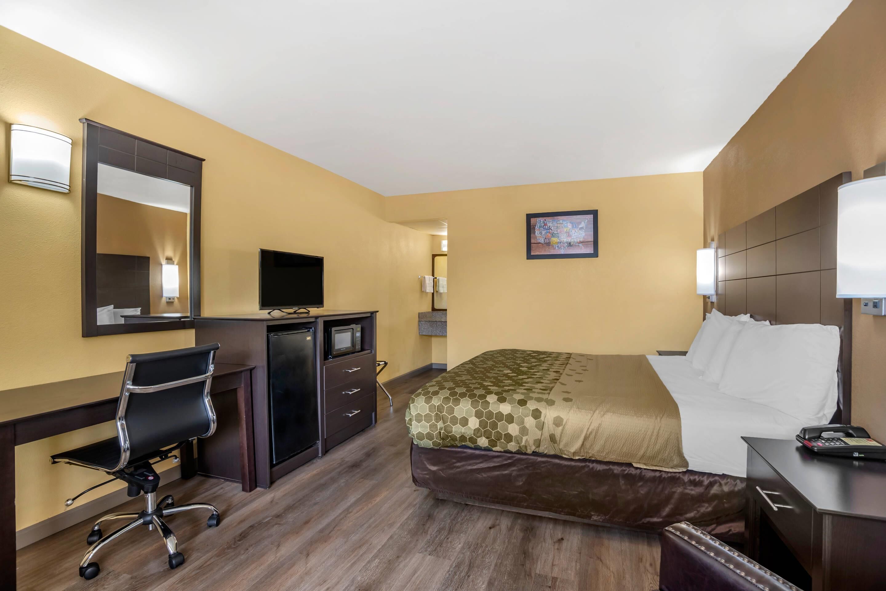 A hotel room with a bed, desk, chair, TV, and a painting on the wall.