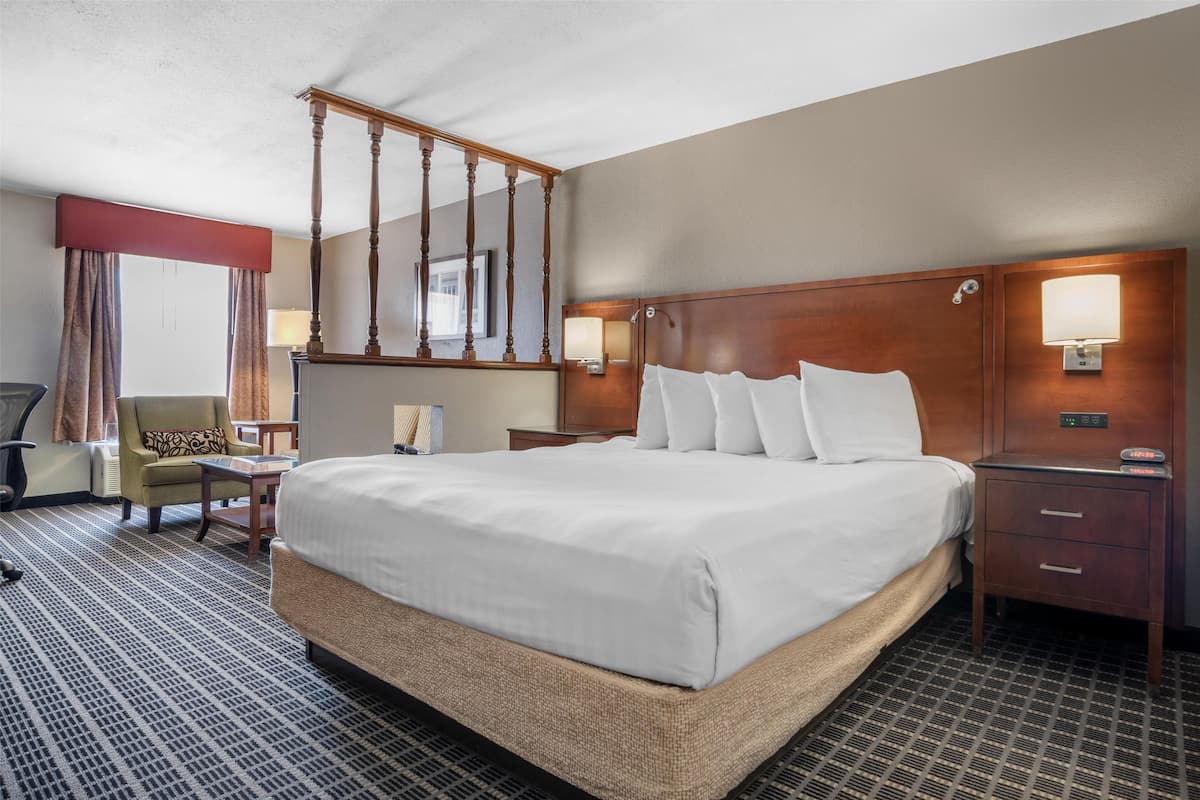 A hotel room with a large bed, a wooden headboard, a nightstand, a desk, a chair, and a window with curtains.