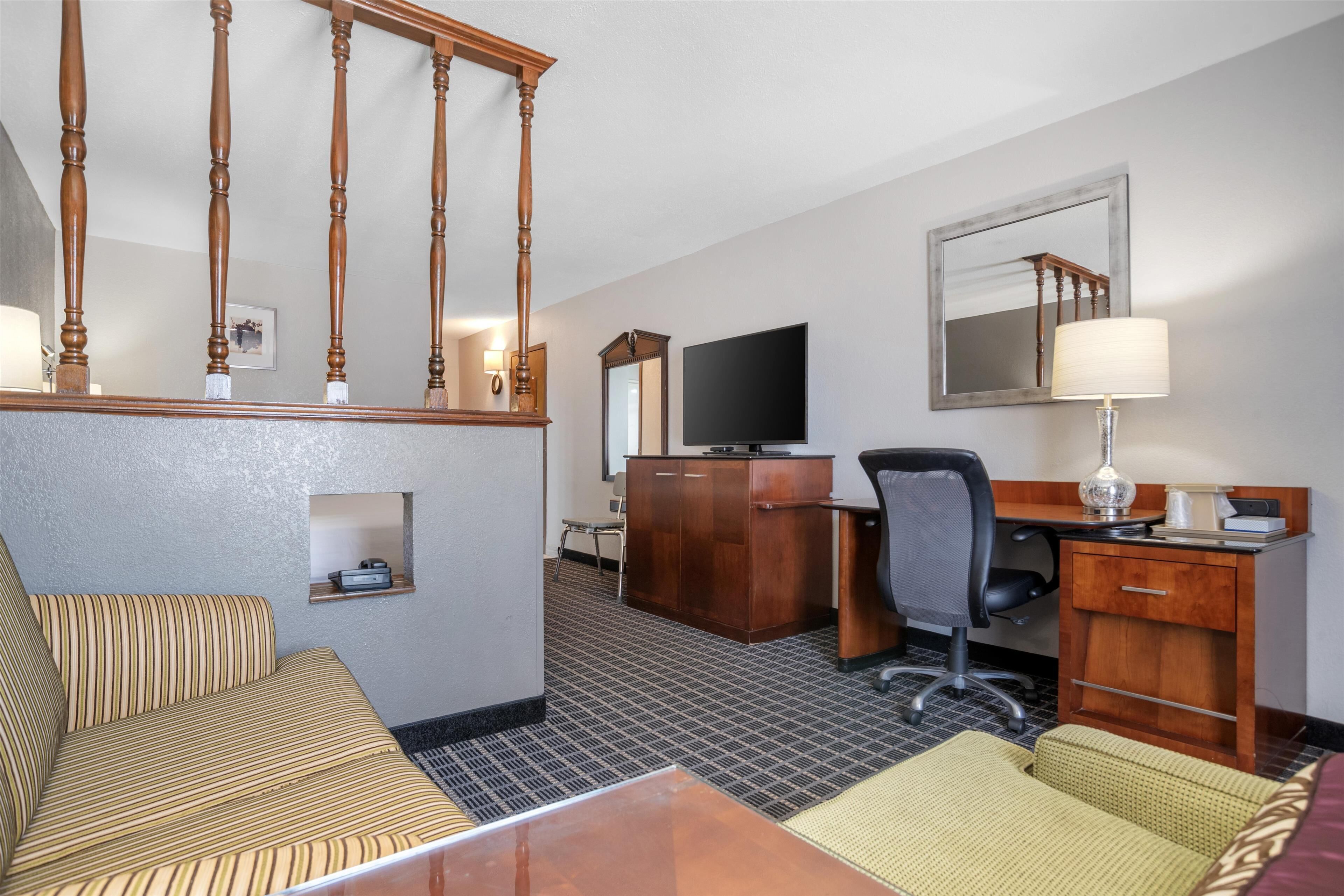 A hotel room with a wooden staircase, a sofa, a desk with a computer, a TV, and a lamp.