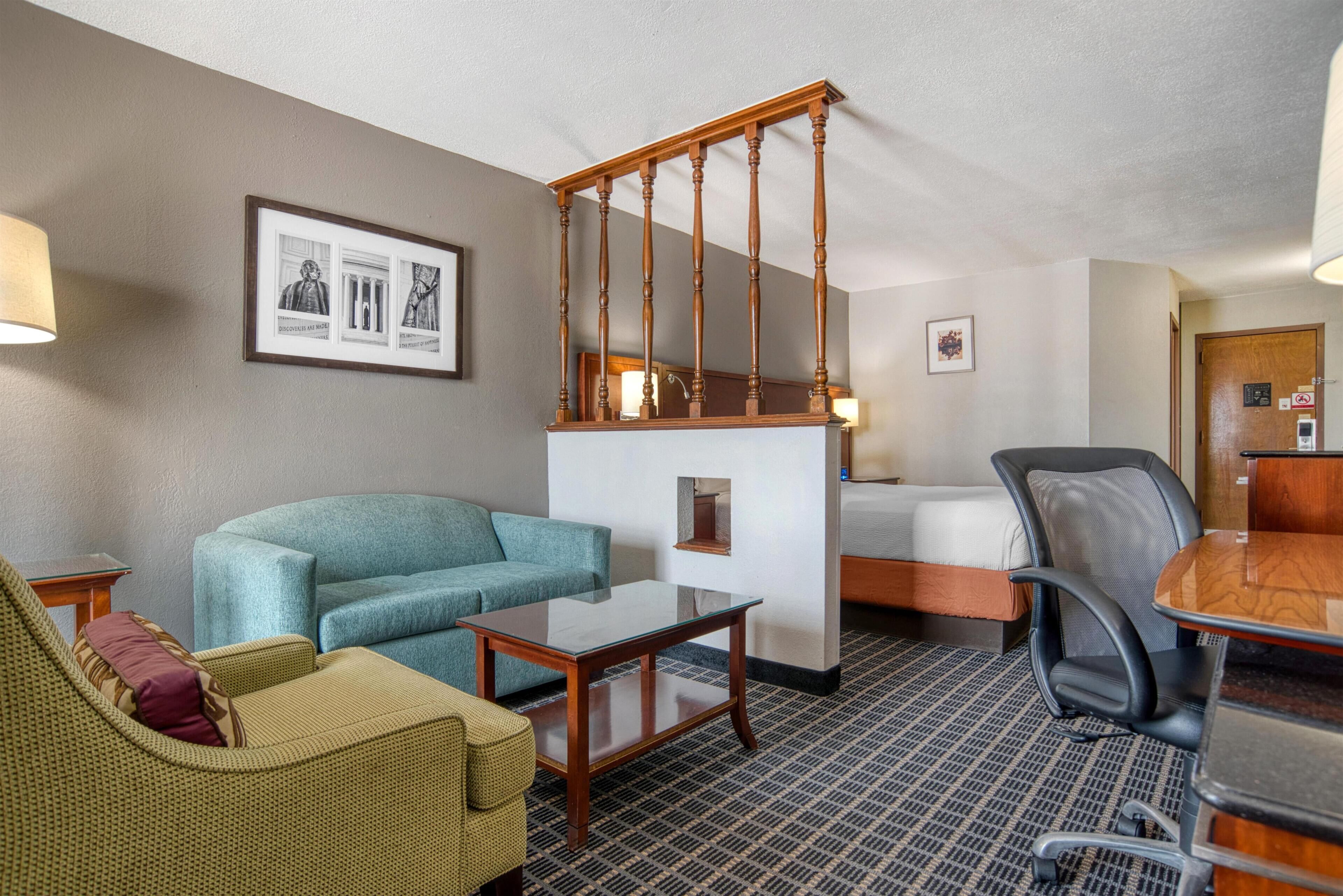 A hotel room with a sofa, armchair, small table, and a bed.
