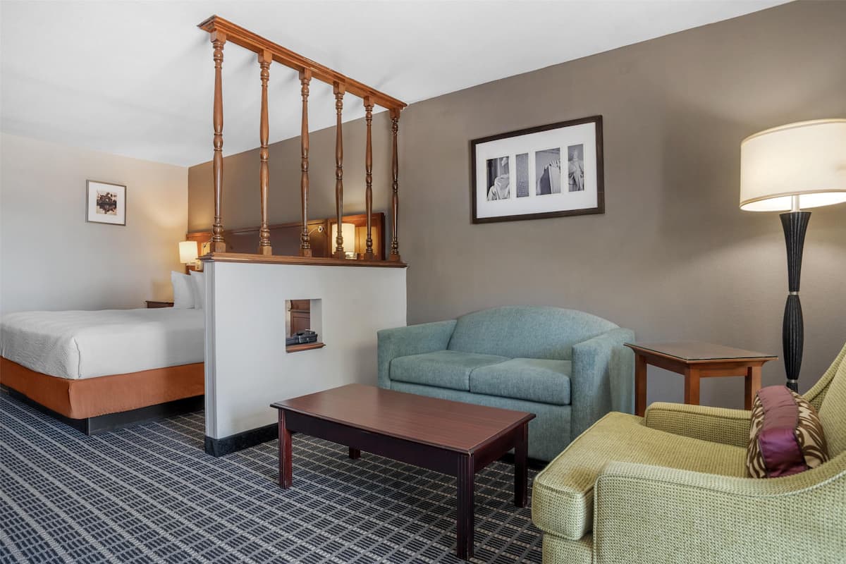 A hotel room with a bed, a sofa, a coffee table, a lamp, a picture frame, and a staircase.