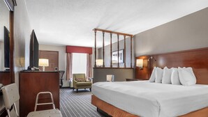 Une chambre d’hôtel avec un grand lit, un bureau, une chaise, un fauteuil roulant et un miroir.