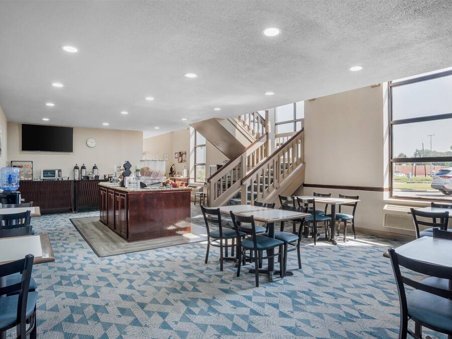 A spacious hotel lobby with a central bar, seating area, and a staircase leading to upper floors.
