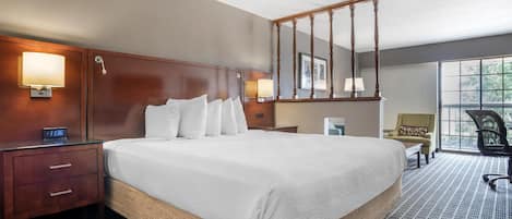 A hotel room with a large bed, wooden headboard, bedside lamps, a desk, and a chair.