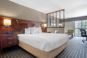 Habitación de hotel con una cama grande, cabecero de madera, lámparas de noche, un escritorio y una silla.