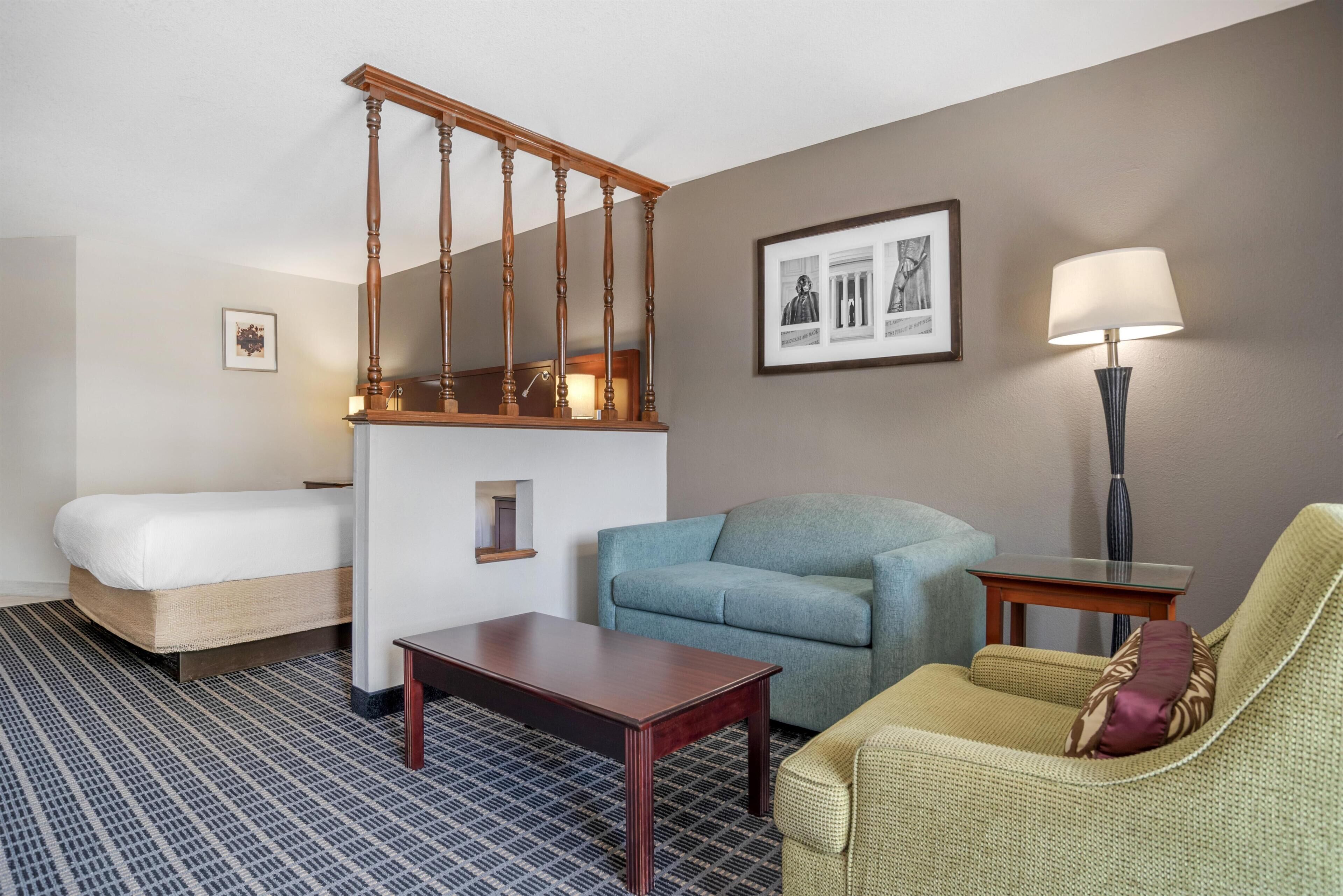 A hotel room with a bed, a sofa, a chair, a small table, a lamp, and a framed picture on the wall.
