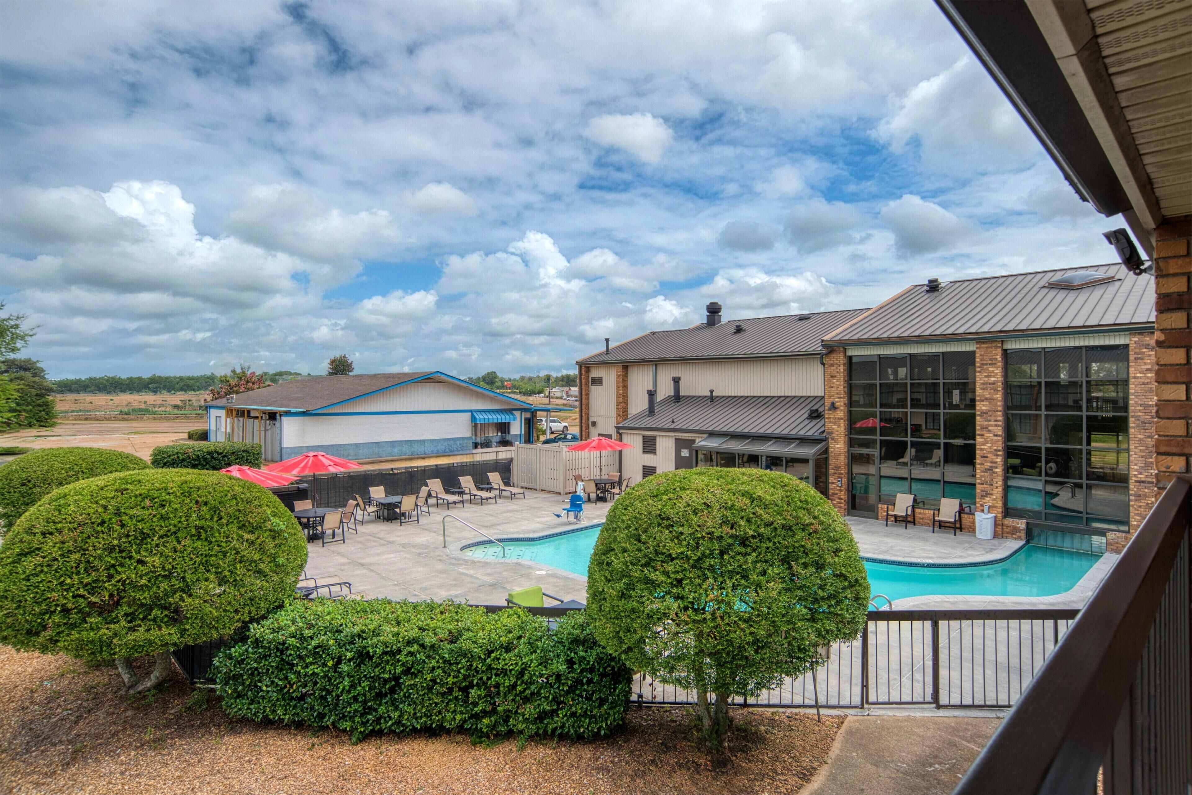 A swimming pool with lounge chairs and umbrellas, surrounded by well-maintained hedges.