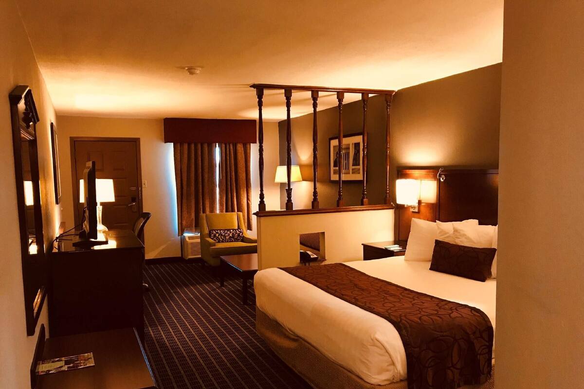 Une chambre d’hôtel comprenant un lit, un bureau, une chaise, une lampe de bureau, un téléviseur fixé au mur et un grand miroir.