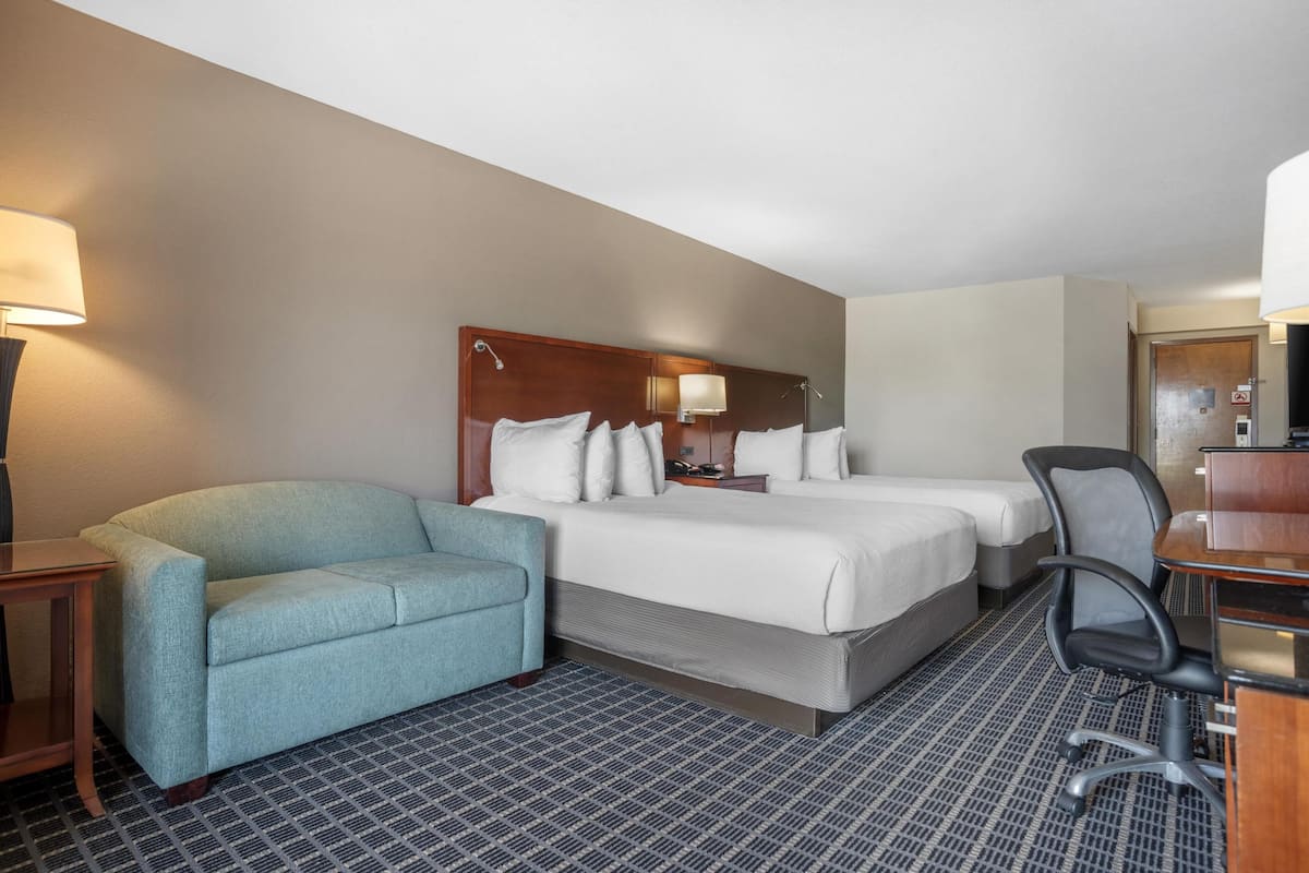 A hotel room with a bed, two bedside tables, a desk, a chair, and a sofa.
