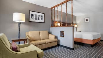 A hotel room with a sofa, a chair, a bed, a staircase, and a lamp.