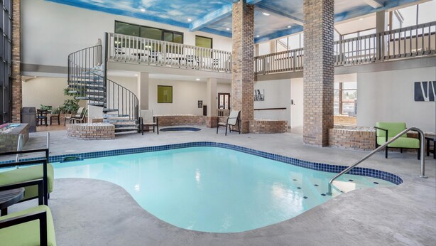 Une piscine intérieure avec une colonne en briques, un escalier et un balcon équipé de chaises.