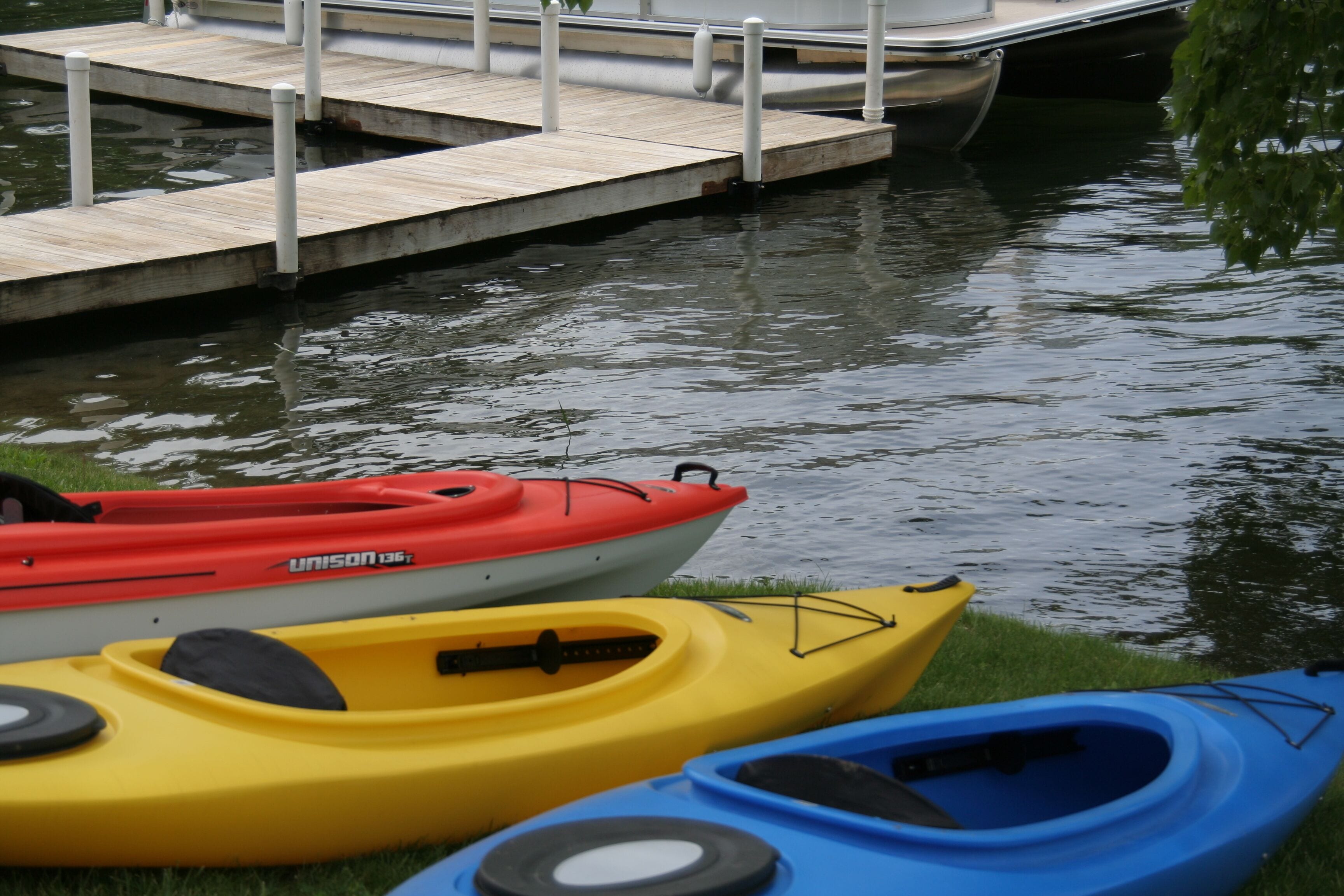 A row of kayaks lined up on a grassy dock by a calm body of water.