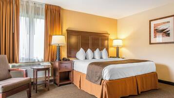 Ein Hotelzimmer mit einem Bett, zwei Nachttischen mit Lampen, einem Sessel, einem Schreibtisch und einem fenster mit Vorhängen.