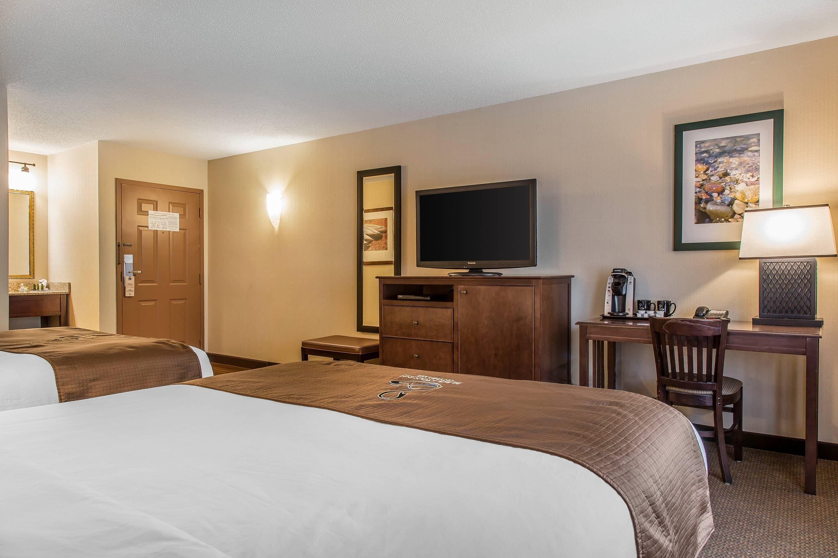 A hotel room with two beds, a desk with a computer, a television, and a coffee maker.