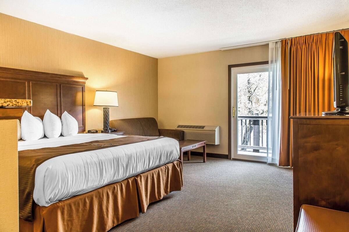 Ein Hotelzimmer mit einem großen Bett, einem Schreibtisch, einem Stuhl, einem Fernseher und einem Fenster mit Vorhängen.