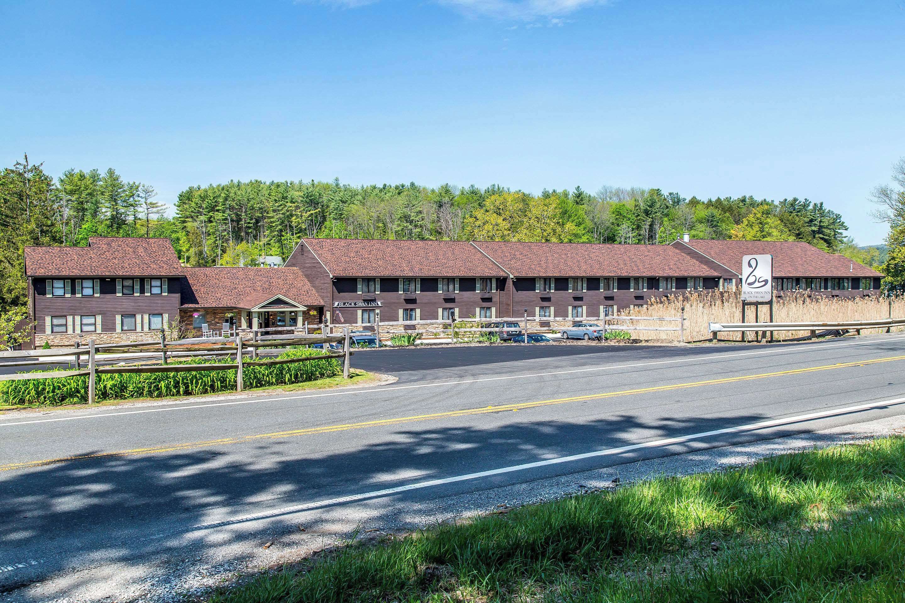 A motel with a central building and two wings, a paved road in front, and a forested backdrop.