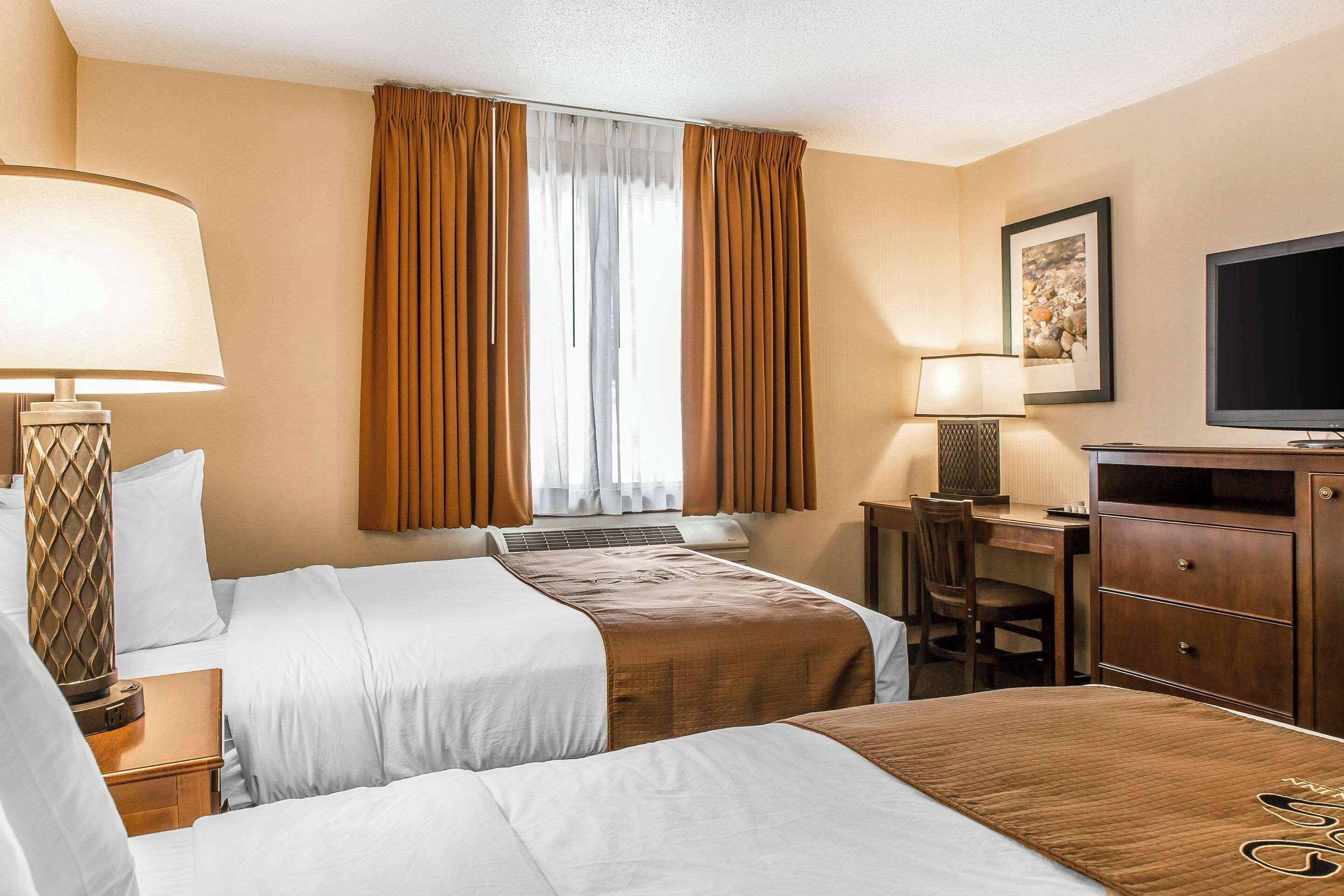 A hotel room with two beds, a desk, a TV, and a window with curtains.