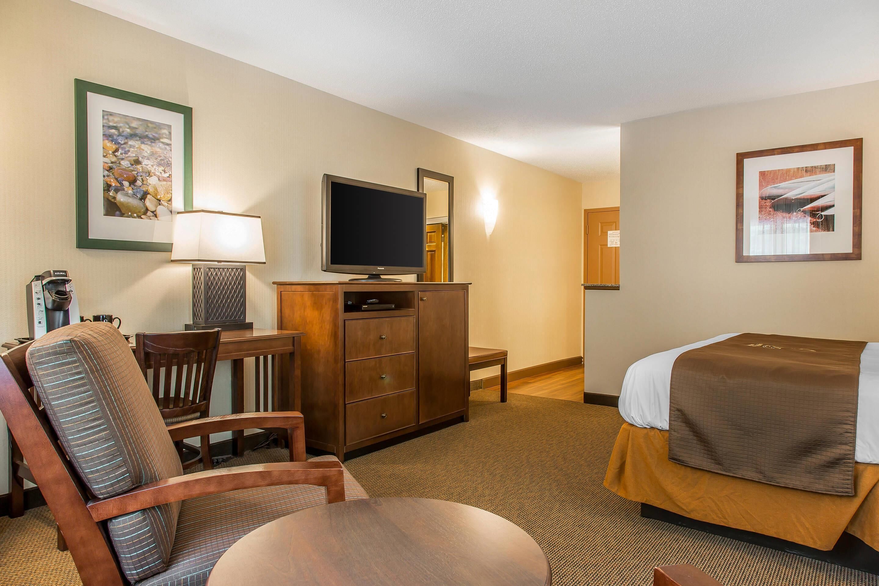 A hotel room with a bed, a desk with a television, a chair, and a dresser.