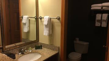 A bathroom with a granite countertop sink, a large mirror, a towel rack with white towels, a toilet, and a towel rack with folded towels.