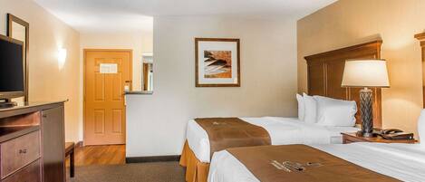 A hotel room with two beds, a desk, a lamp, and a TV.