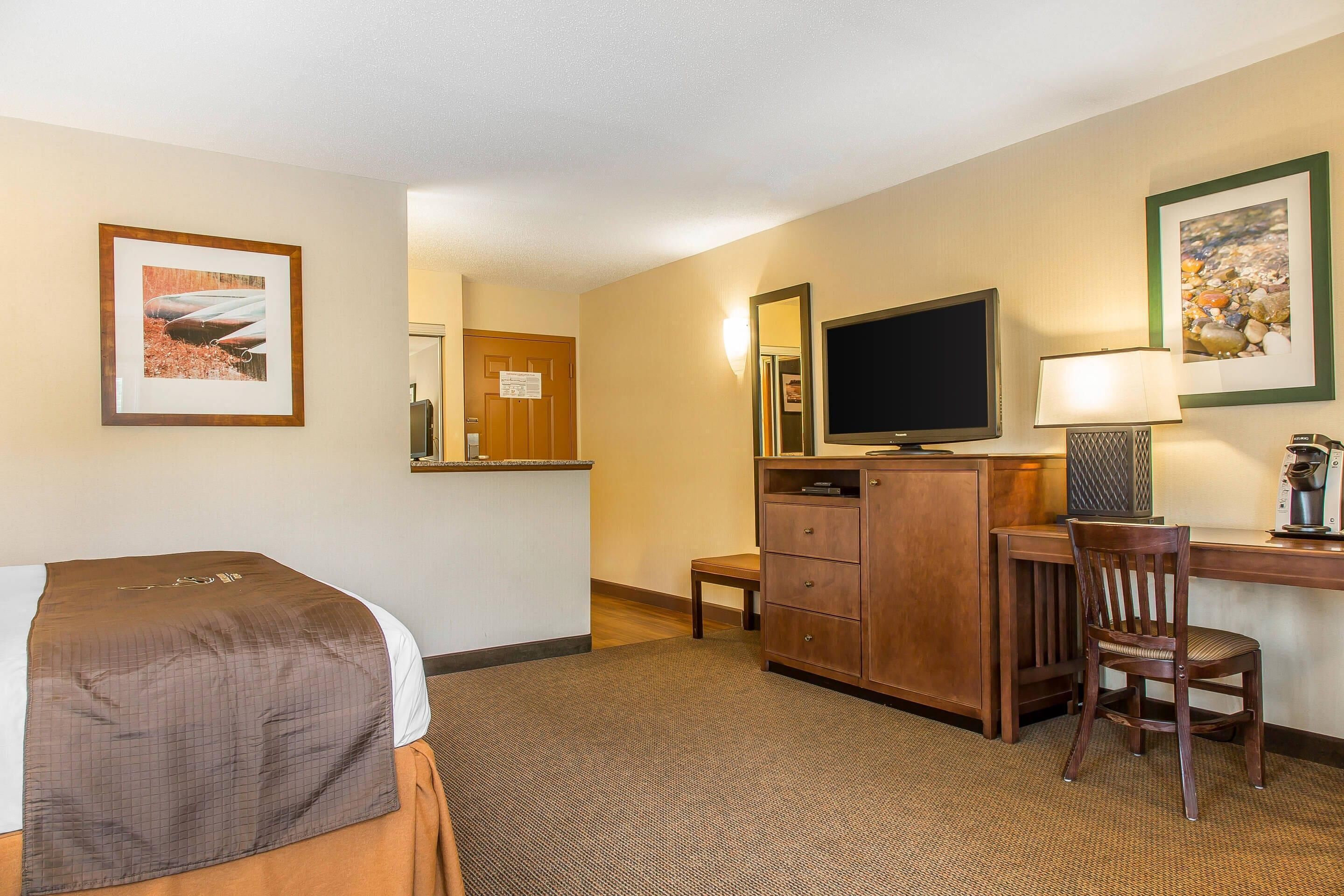 A hotel room with a bed, a desk, a chair, a television, and a dresser.