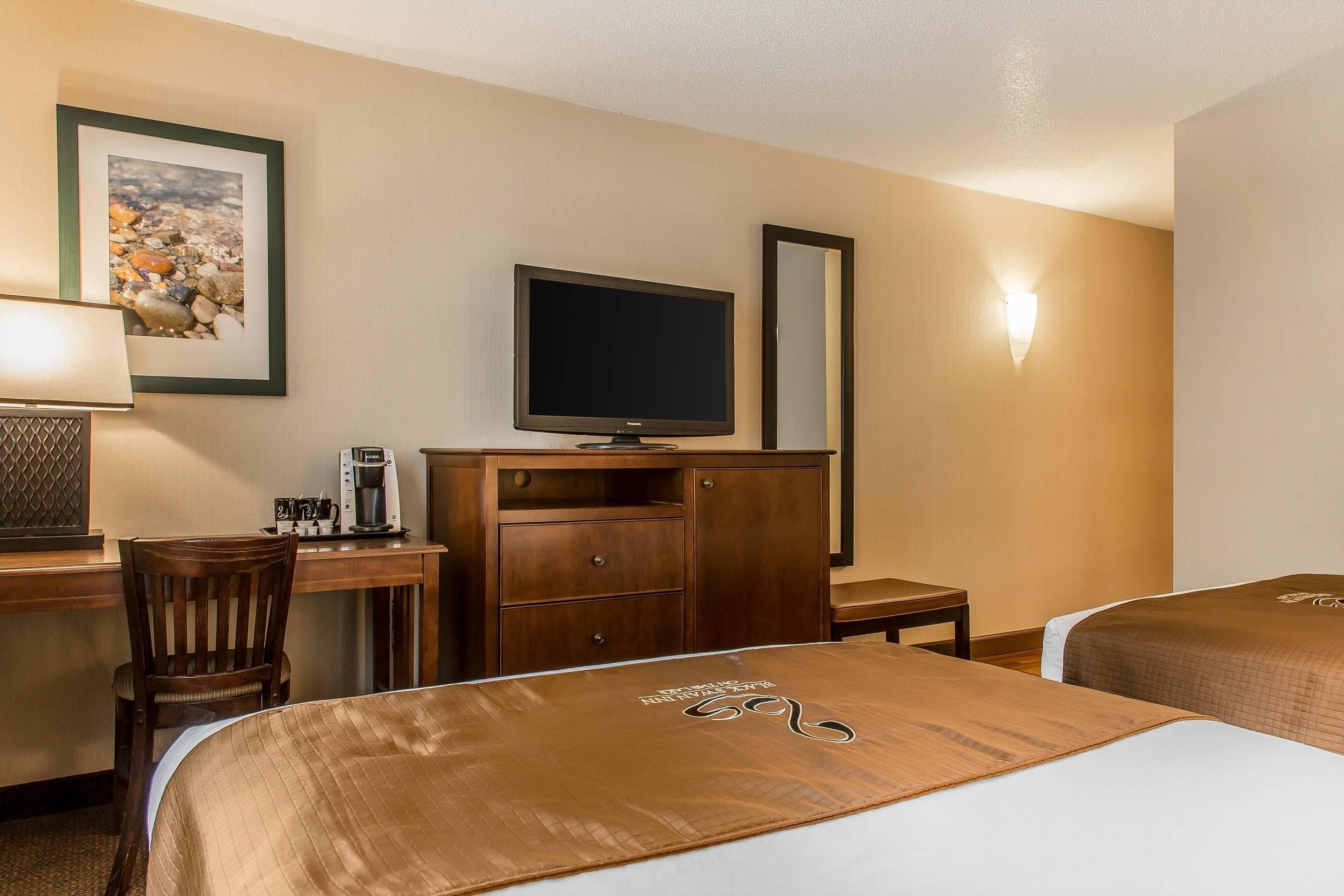 A hotel room with two beds, a desk with a television, a coffee maker, and a framed picture on the wall.