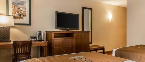 A hotel room with two beds, a desk with a television, a coffee maker, and a framed picture on the wall.