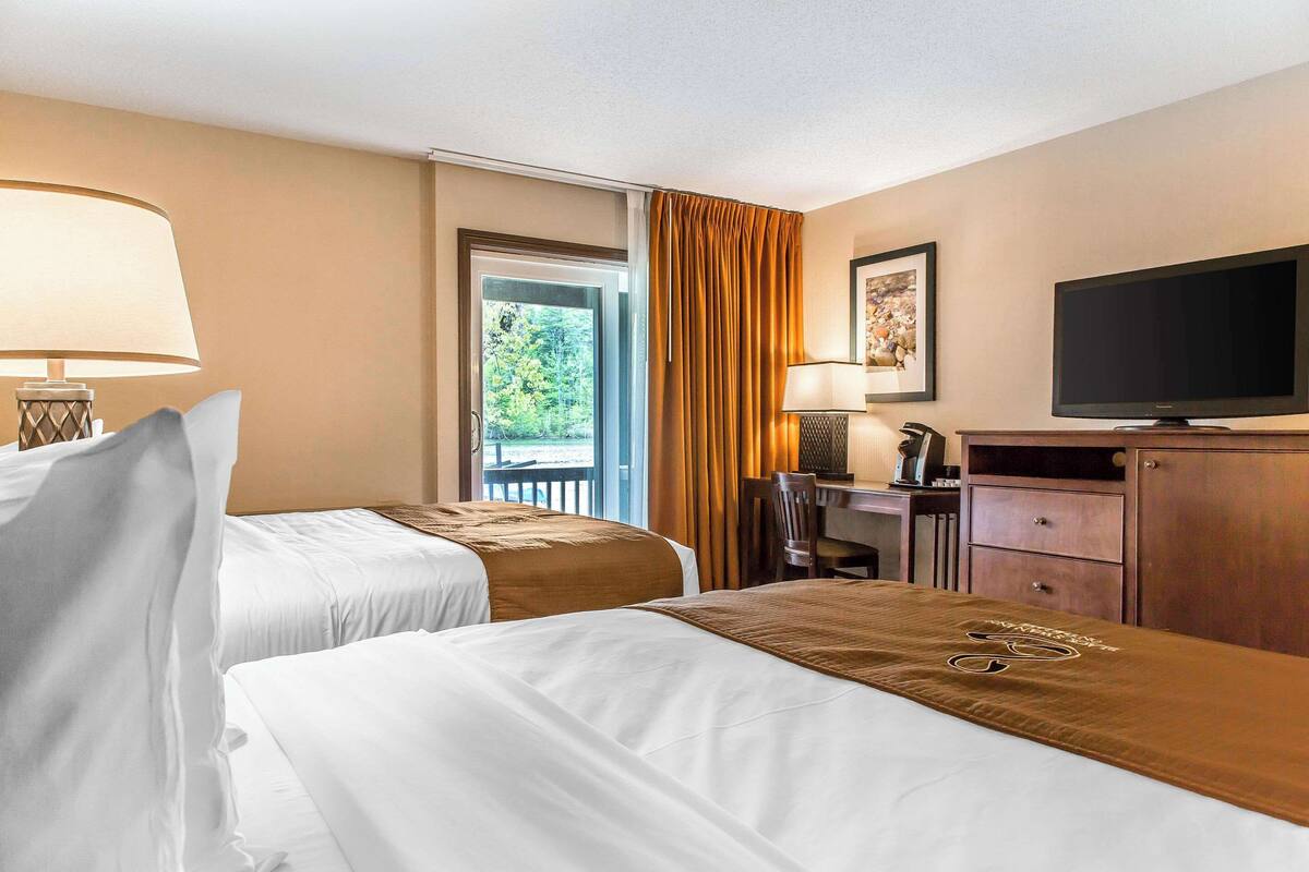 Ein Hotelzimmer mit zwei Betten, einem Schreibtisch, einem Fernseher und einem Fenster mit Vorhängen.